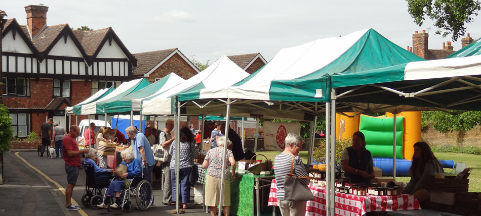 Wye Farmers' Market, The Green with shoppers buying from stalls of local produce and a bouncy castle