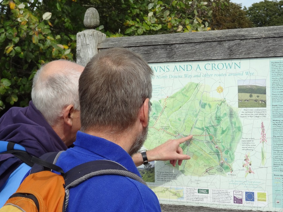 Two walkers on the North Downs Way National Trail consult the map in Wye churchyard